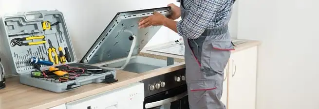 Cooktop repair technician lifting a built-in stovetop for service in Chicago, IL