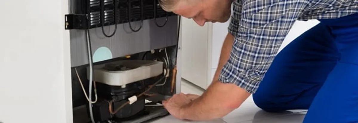Refrigerator repair technician servicing the compressor and condenser area in Chicago, IL
