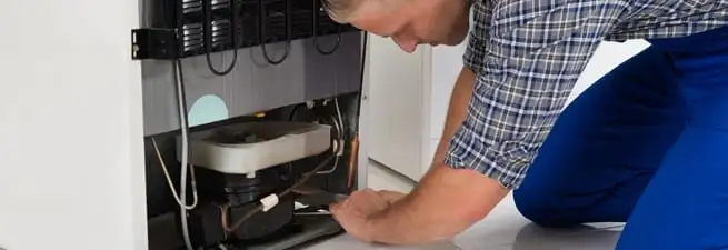 Refrigerator repair technician servicing the compressor and condenser area in Chicago, IL