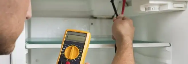 Refrigerator repair technician testing electrical components with a multimeter in Chicago, IL