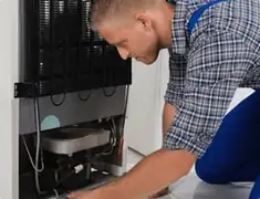 Refrigerator repair technician servicing the compressor and condenser area in Chicago, IL